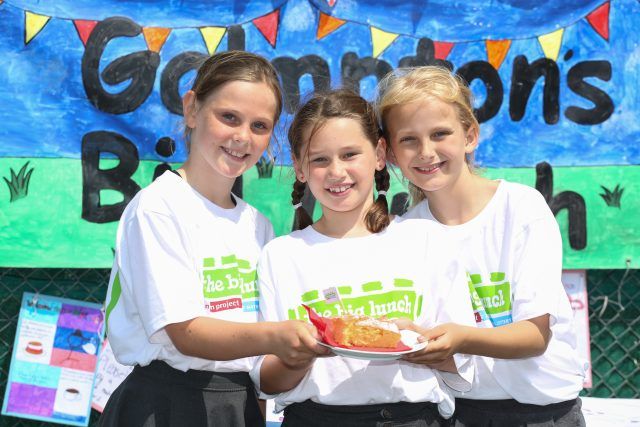 Three girls hold up a plate of cake wearing Big Lunch tshirts