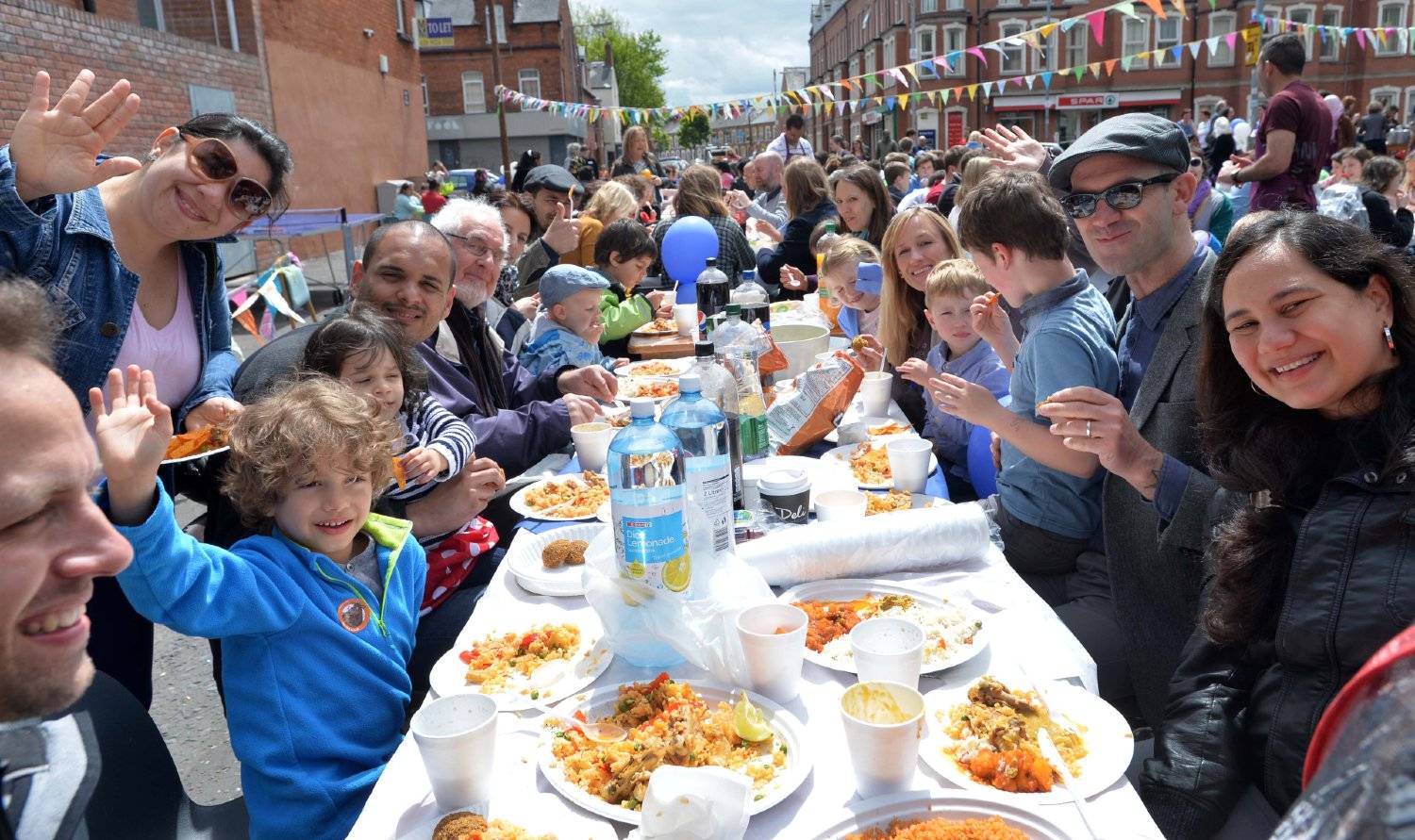 Group of people around a table outside smiling with their hands in the air for the Belfast City Church Big Lunch