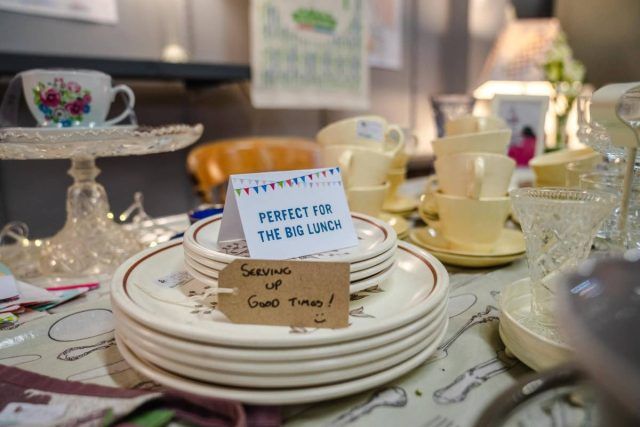 Pile of plates in a charity shop with a 'Perfect for The Big Lunch' sign on top.