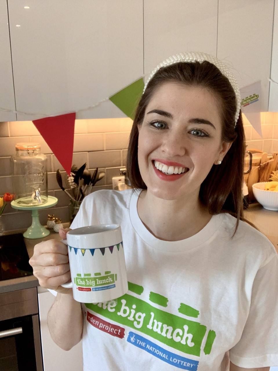 Alice Fevronia smiling in the kitchen wearing a Big Lunch t-shirt and holding a big lunch mug