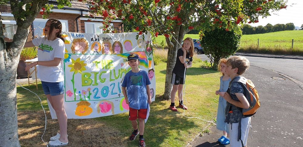 Children hanging 'The big Lunch' poster between two trees