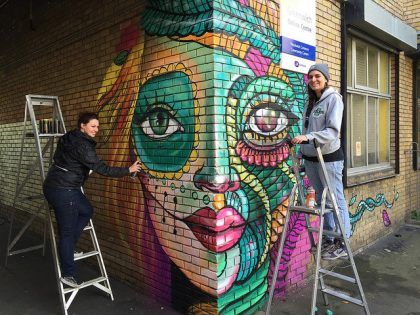 Two women Graffitiing woman's face on a brick wall