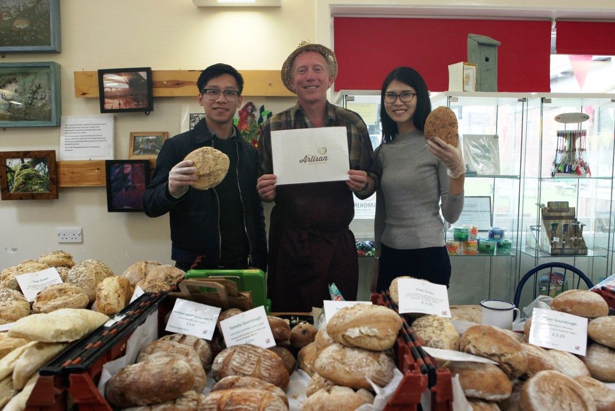 three people holding bread with crates of bread in front of them