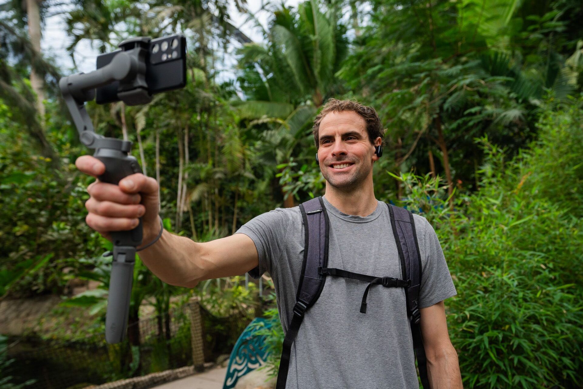 A man holds a selfie stick with a camera towards him. He's standing in the Rainforest biome.