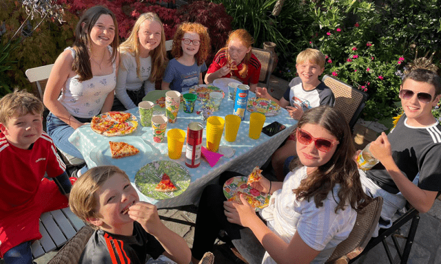 Children eating pizza around a table in a garden
