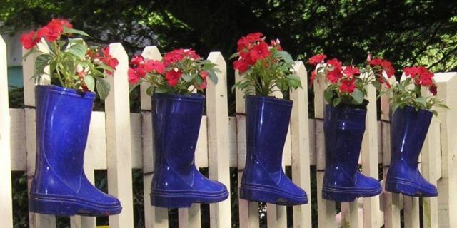 Wellington boots with flowers inside attached to a garden picket fence