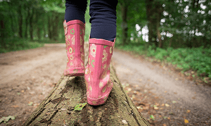 girl walking on tree trunk with wellies
