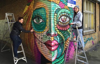 Two women Graffitiing woman's face on a brick wall