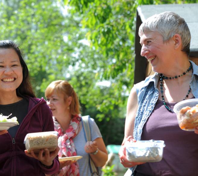 Two ladies laughing and carrying food containers to a Big Lunch.