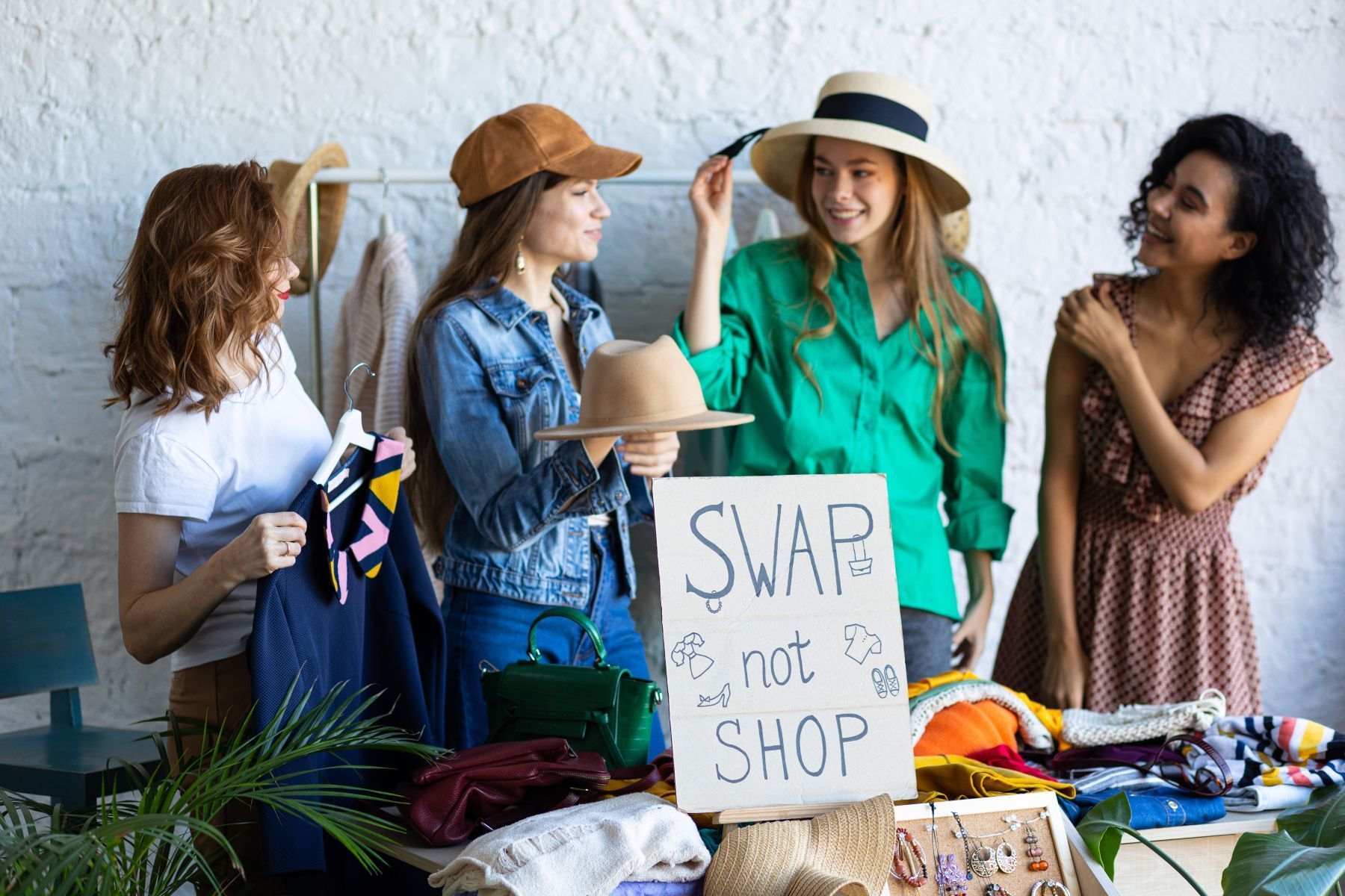 A group of women trying on clothes in front of a sign that says 'Swap don't shop'