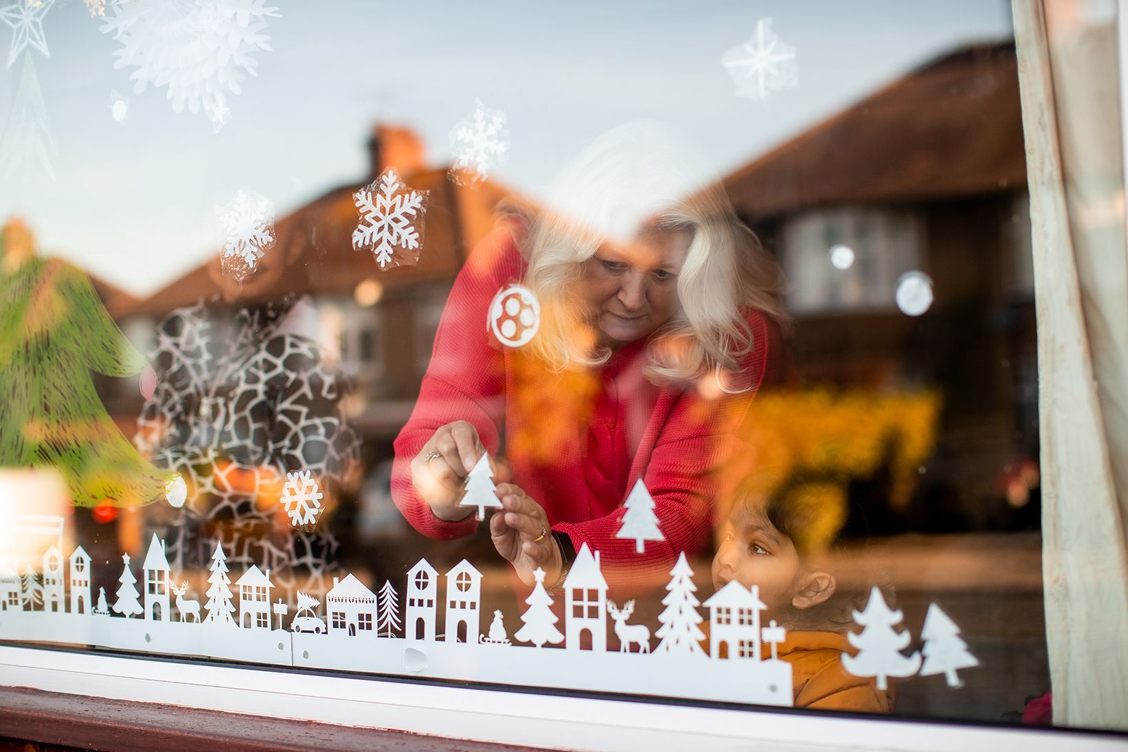 A woman adding the final touches to her advent window - you can see a paper strip of houses along the bottom with paper snowflakes and trees above it.