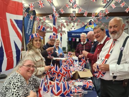 Jubilee Big Lunch celebrations with Morecombe Town Council. A group are gathered and smiling, waving British flags with bunting.