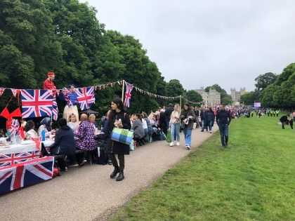 A street party on the grounds at Windsor Castle to celebrate the Queens Jubilee. There are British flags and bunting with people gathering and sat at tables sharing lunch.