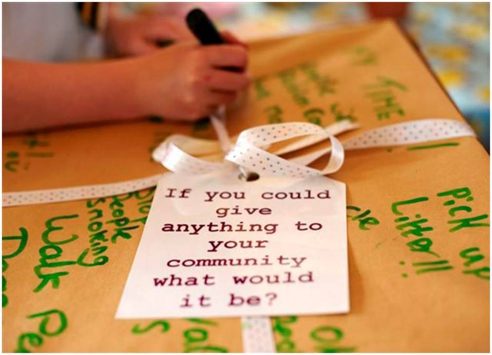 Box with tag saying 'If you could give anything to your community, what would it be?'. In the background, someone is writing and you can see the text 'Pick up litter!' visible.