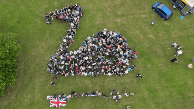 Group of people arranged together so the photo from above shows a swan and a Union Jack