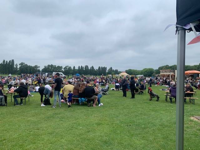 Groups of people socialising around tables on a grass field in cloudy weather