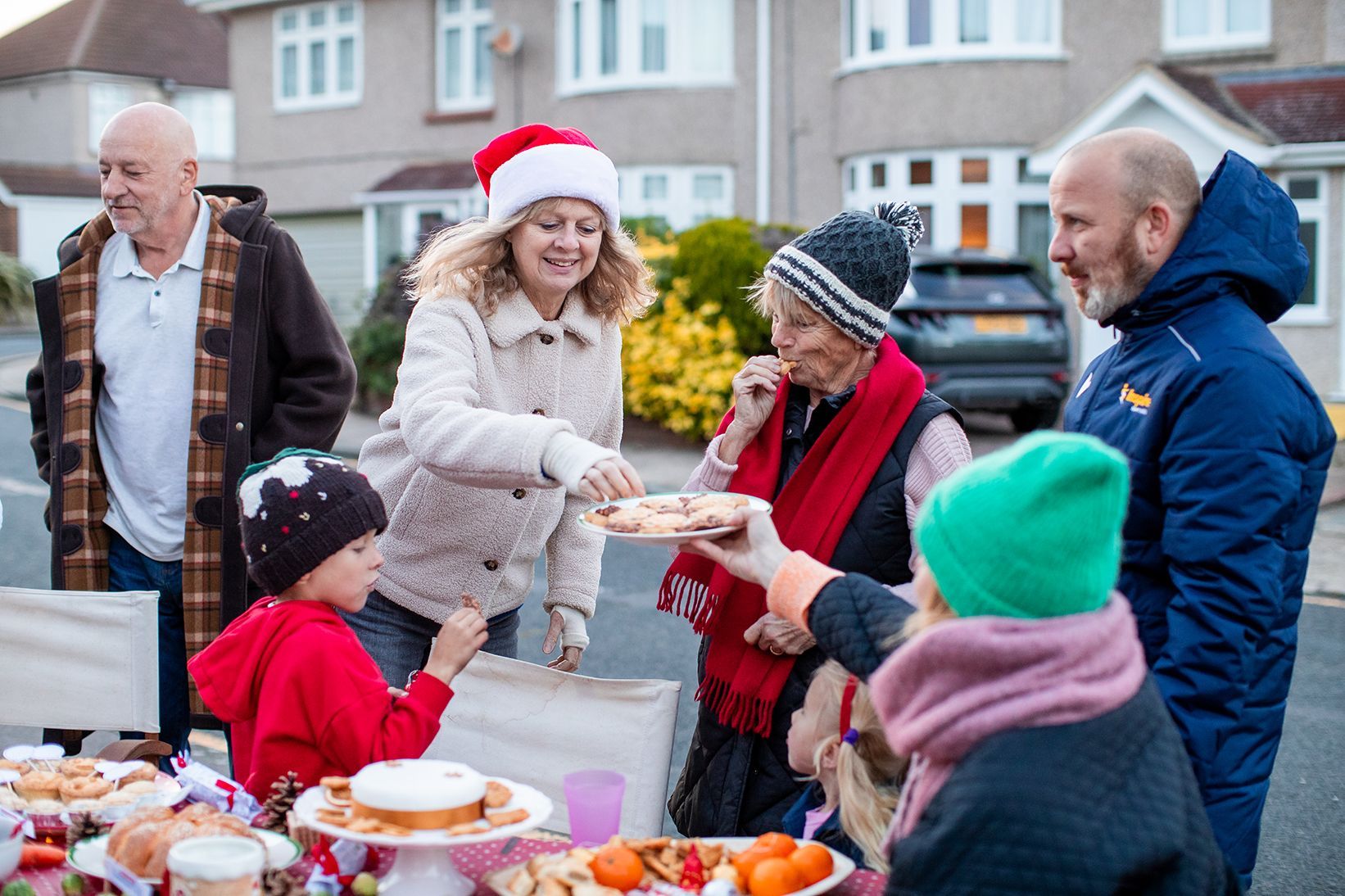 A group of people stand outside, all bundled up warm. They're sharing food and smiling.