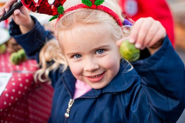 A little girl smiling and holding up a sprout