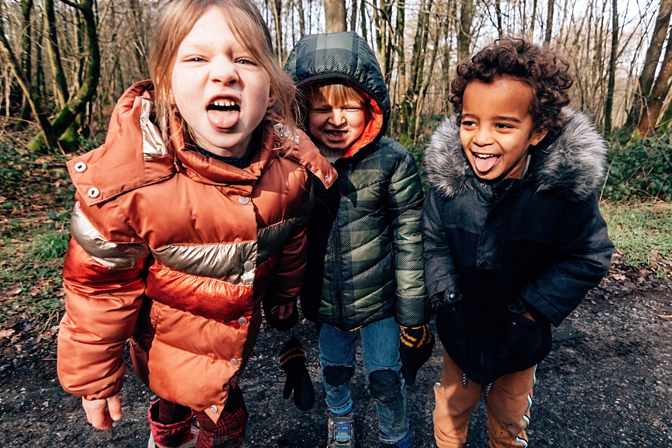 Three children huddled in coats stick their tongues out at the camera