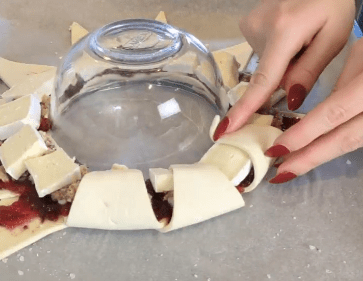 Folding up pastry triangles over the cranberry sauce, stuffing and brie to form a wreath shape