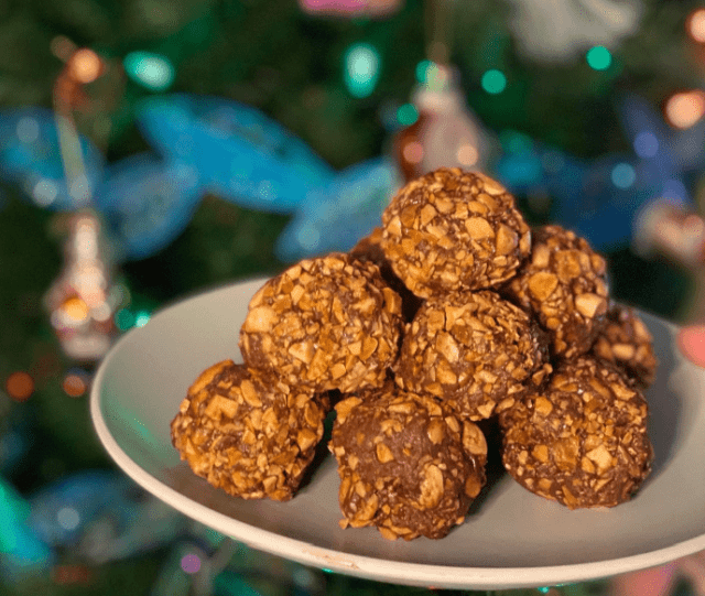 Chocolate festive truffles rolled in nuts by Bake Off's Lizzie Acker. Christmas tree lights sparkle in soft focus in the background.