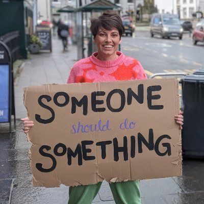 Kathryn Welch holding a sign that says 'someone should do something'