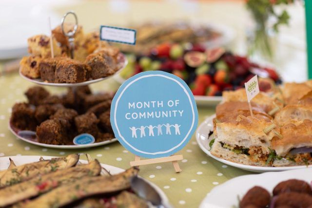 Cakes spread out on a table with the Month of Community logo resting against them.