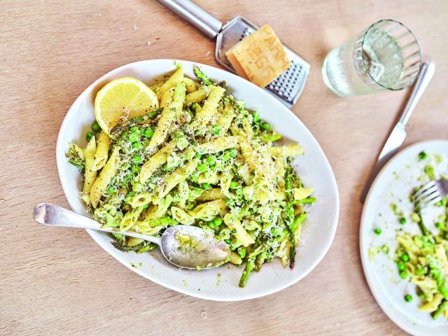 Spring vegetable pasta with a slice of lemon in a large serving dish