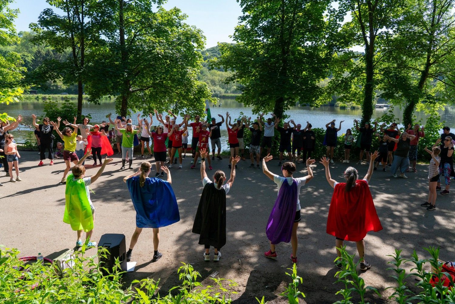Two lines of people (one wearing capes) all raise their hands at each other as part of a series of battle games