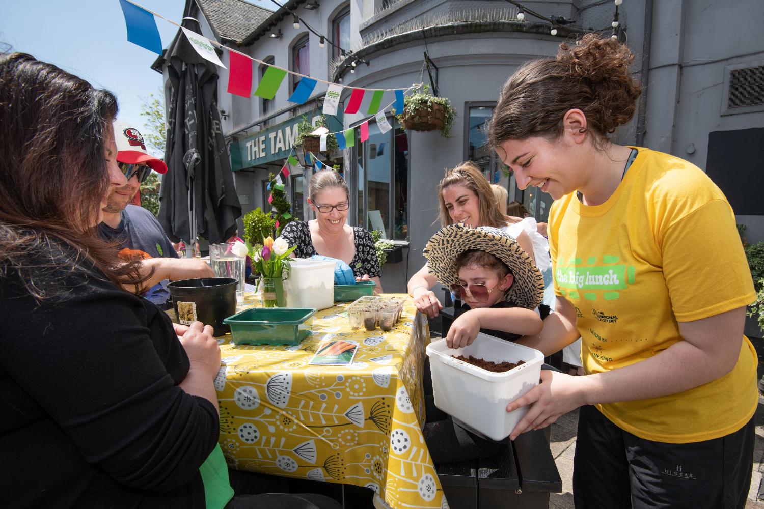 A group of people sow seedlings outside a pub. They're all smiling and bunting is hanging in the background