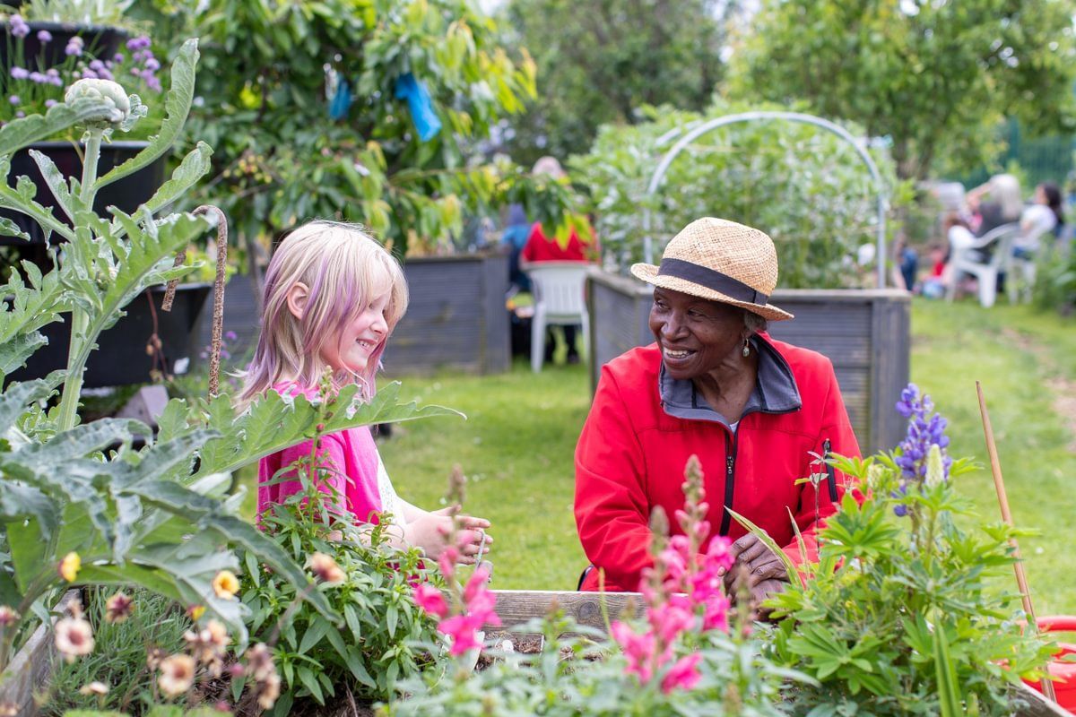 A woman and a child gardening together at a community Big Lunch. They're smiling and look happy. The older woman is sharing her gardening skills with the child.