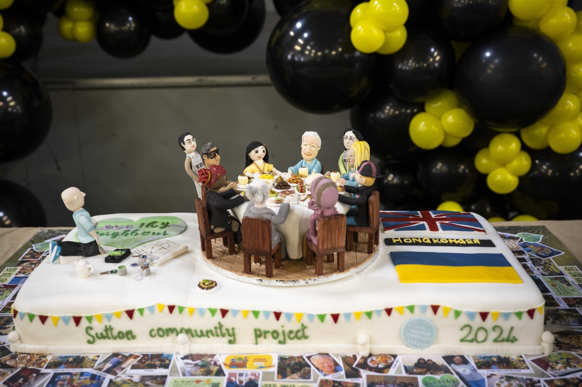 A handmade cake of volunteers from Sutton Community Project having a Big Lunch. The cake has edible models of 9 people sitting around a round table with a food buffet.