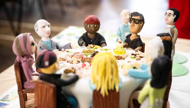 A handmade cake of volunteers from Sutton Community Project having a Big Lunch. The cake has edible models of 9 people sitting around a round table with a food buffet.