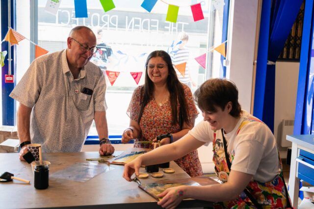Three people stand round a table smiling. One of them is clipping something onto a clipboard.