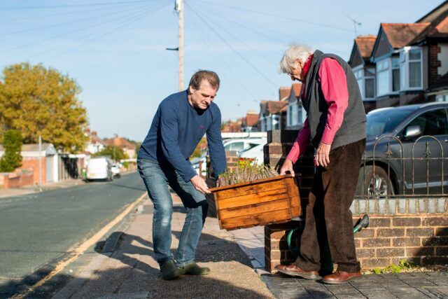 Two men carry a planter of herbs between them