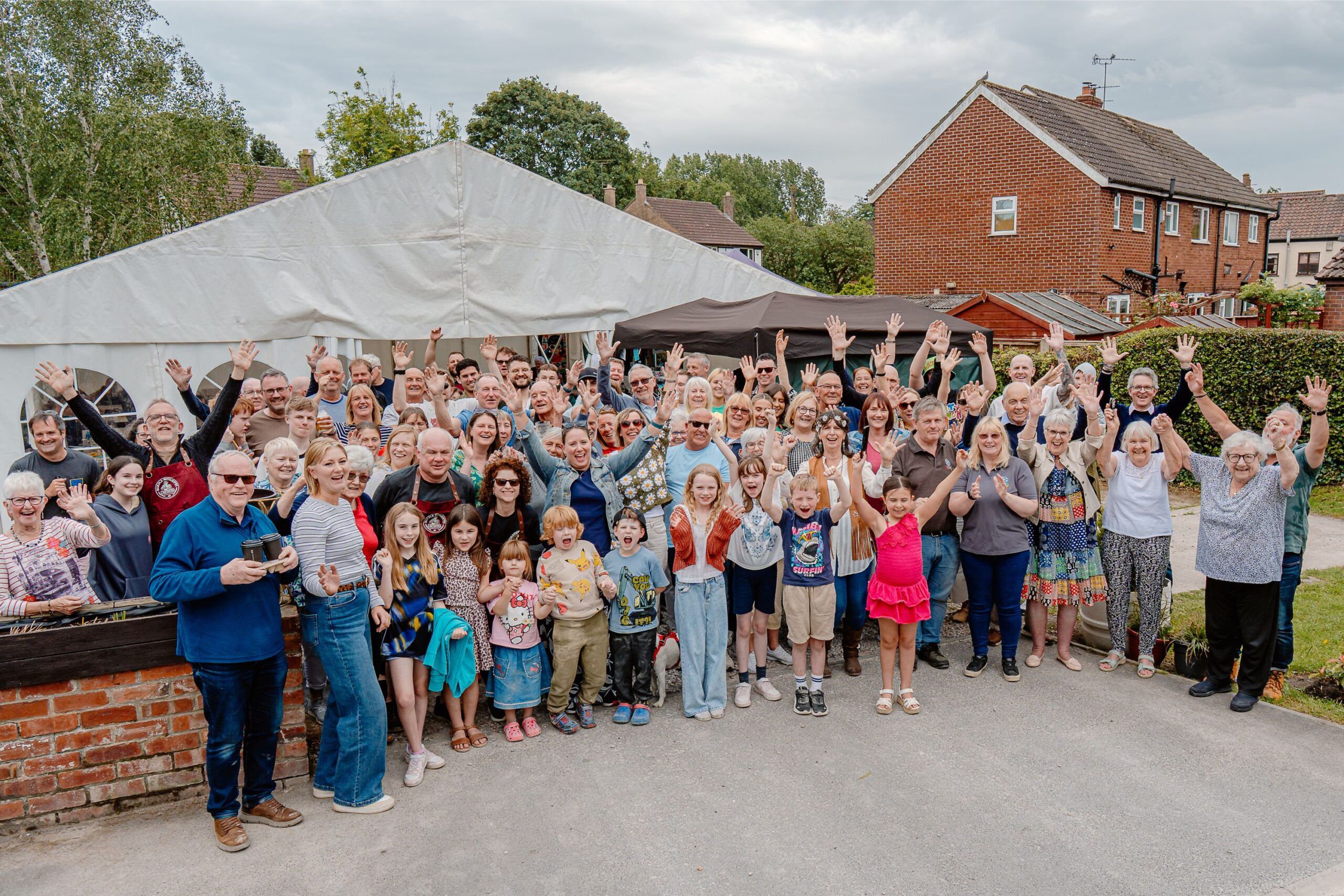 A huge group of people standing in front of a marquee and waving at the camera